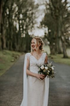 a woman in a wedding dress is standing on the road and smiling at the camera