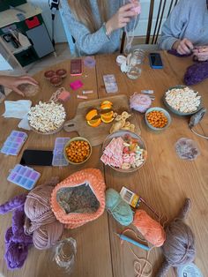 two women sitting at a wooden table with yarn and other items on the table top