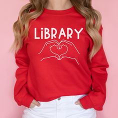 a woman wearing a red library sweatshirt with two hands in the shape of a heart