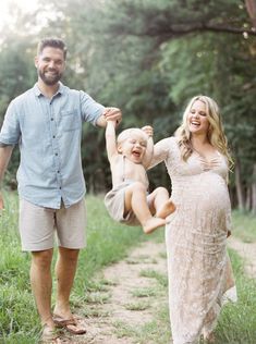 a man and woman holding a baby in the air while walking down a dirt path