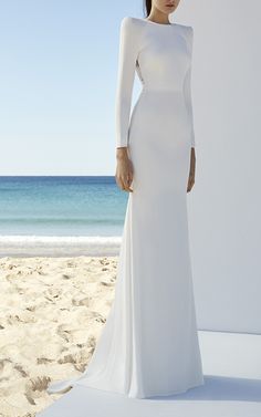 a woman standing on top of a beach next to the ocean wearing a white dress