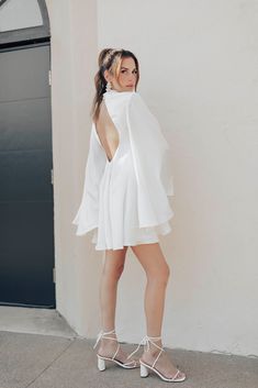 a woman in a white dress is standing on the sidewalk wearing high heels and a shawl