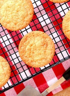 several cookies cooling on a wire rack with a spatula next to it and a red checkered tablecloth