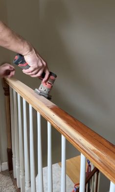 a man sanding the bannister with a power drill