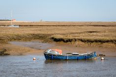 a blue boat sitting on top of a body of water next to a dry grass field