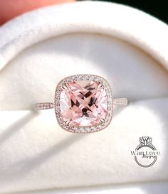 a pink diamond ring sitting on top of a white cloth covered cushioned pillow in a box