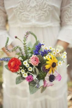 a woman in a white dress holding a bouquet of wildflowers and daisies