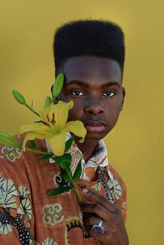 a young man holding a yellow flower in his right hand and looking at the camera