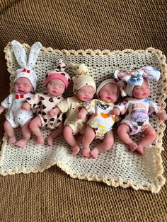 five baby dolls laying on top of a blanket next to each other in different outfits