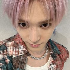 a young man with pink hair wearing a plaid shirt and silver chain around his neck