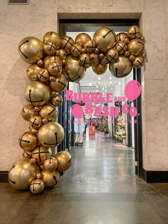 a large balloon arch in the middle of a hallway with gold balloons hanging from it's sides