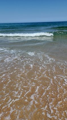 the ocean waves are rolling in and out on the shore line with blue skies above