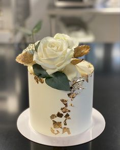 a white and gold decorated cake with flowers on the top is sitting on a table