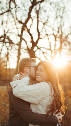 a man and woman hugging each other while the sun is setting in the sky behind them