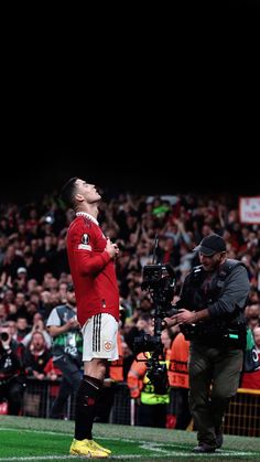 a man standing on top of a soccer field next to a cameraman in front of a crowd