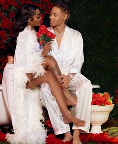 a man and woman sitting next to each other in front of red flowers on the ground