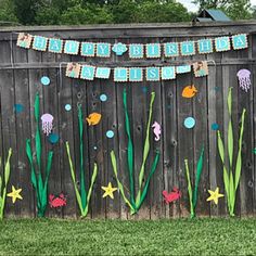 a birthday banner on a fence with seaweed and jellyfish in the grass next to it