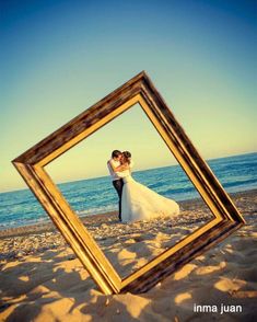 a bride and groom standing in the sand with their arms around each other