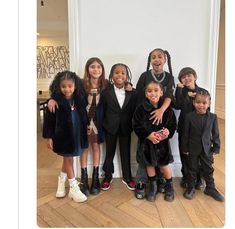 a group of children standing next to each other in front of a white wall and wooden floor