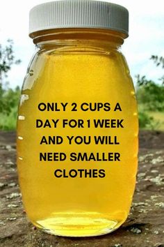 a jar filled with yellow liquid sitting on top of a dirt ground next to trees