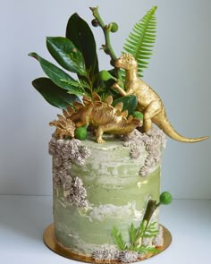 there is a green cake decorated with gold dinosaurs and plants on it's side