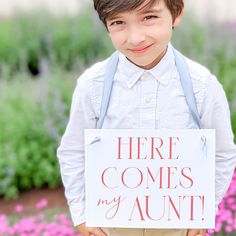 a young boy holding up a sign that says here comes my aunt with flowers in the background