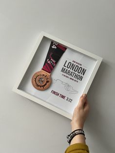 a person holding up a medal in front of a white frame with the london marathon logo on it