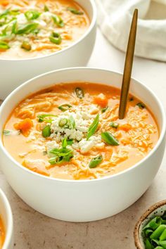 two white bowls filled with soup and topped with green onions, carrots and cheese