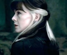 a woman with blonde hair and earrings looking off to the side in a dark forest