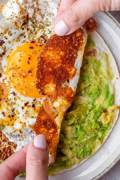 a person is holding an egg over some tortilla and guacamole