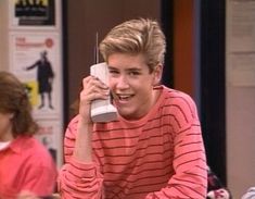 a young man talking on a phone while sitting at a table in front of a tv