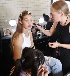 a woman is getting her make up done while another girl looks on in the mirror