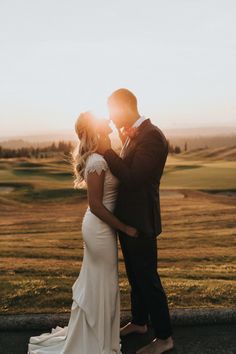 a bride and groom kissing in front of the sun on their wedding day at sunset