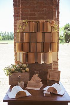 an arrangement of books on a table in front of a brick wall with flowers hanging from it