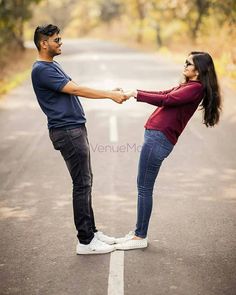 a man and woman holding hands while standing in the middle of an empty road with trees behind them