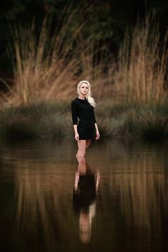 a woman standing in the middle of a body of water with tall grass behind her