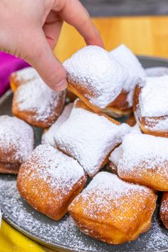 powdered sugar covered donuts on a plate being held by a person's hand