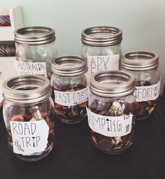 there are many glass jars with coins in them on the table and one has a sign that says road trip