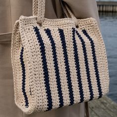 a crocheted handbag is being held by a woman's arm as she stands next to the water