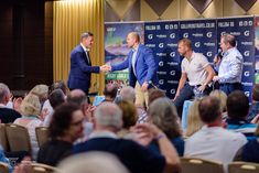 three men shaking hands in front of an audience