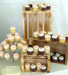 cupcakes are arranged on wooden crates and placed in front of the cake table