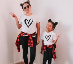 model matching with daughter wearing black hollow heart vinyl print on a white t shirt. mother and daughter with pigtail buns  making silly faces at the camera . both model and mini model dressed up t shirt wearing matching black pants and a red and black checker flannel around the waist. Mommy And Me Christmas Shirts, Mama And Mini Shirts, Mommy And Me Christmas, Mini Shirts, Mama And Mini, Mommy And Me Shirt, Look Short, Mommy And Me Outfits, Heart Shirt