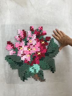 a person holding up a piece of art made out of perler beads with flowers on it