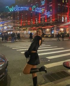 a woman in short skirt and boots standing on the street with her legs spread out