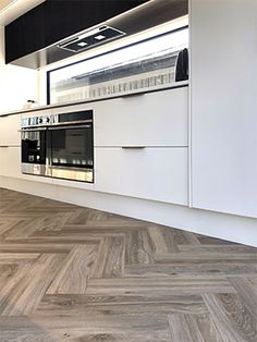 a kitchen with white cabinets and wood flooring next to an oven, microwave and window