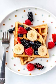 a white plate topped with waffles covered in sliced bananas and raspberries