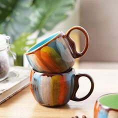 two coffee mugs sitting on top of a wooden table next to a cup filled with coffee beans