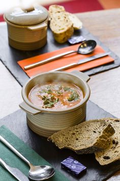 a bowl of soup on a table with bread and spoons