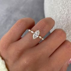 a woman's hand with a diamond ring on top of her finger, wearing a white sweater