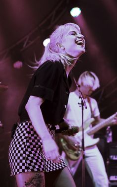 a woman singing into a microphone while standing next to a man with a guitar on stage